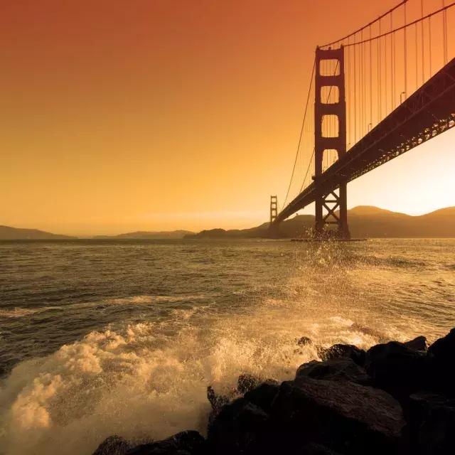 Las olas rompen cerca de Fort Point debajo del puente Golden Gate al atardecer.